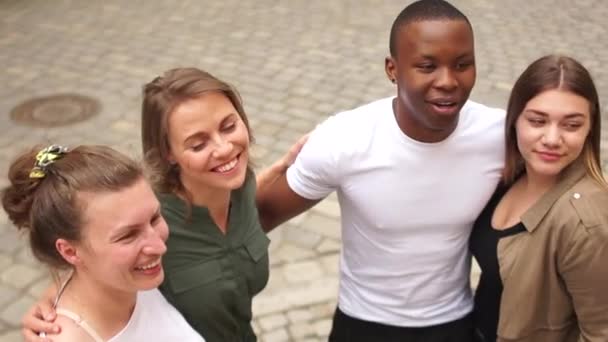 Gruppo multietnico. Quattro giovani studenti si abbracciano e ridono. Vista dall'alto, ritratto esterno, gruppo multirazziale di persone — Video Stock