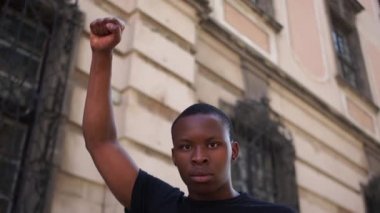 Afrikalı Amerikalı öğrenci ırkçılığı ve şiddeti protesto etmek için yumruğunu sıktı. Açık havada siyah tişörtlü genç bir zenciyi şımartıyor.