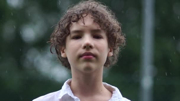 Un garçon triste se mouille sous la pluie. Problèmes psychologiques des adolescents, portrait en plein air d'un adolescent bouclé sous la pluie d'été — Video