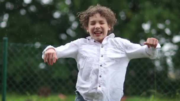Прогноз погоды, счастливое детство. Странный школьник радуется и прыгает под летним дождем. Мальчик в белой рубашке обнимает руки, вытянутые под каплями дождя . — стоковое видео