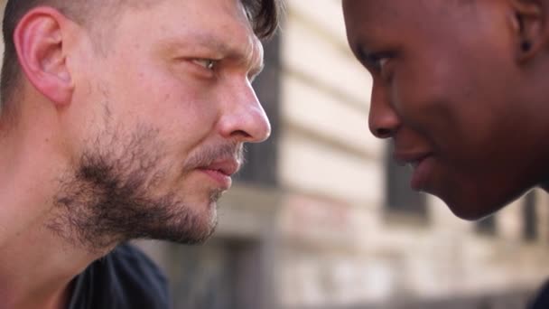 Outdor close retrato de jovens estudantes. Vista lateral. Homem negro e homem branco abraçando e sorrindo. Igualdade, conceito de cumplicidade de amizade. Sem racismo — Vídeo de Stock