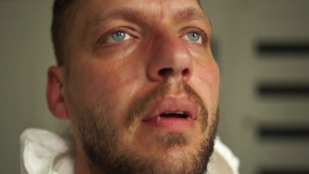 Dicht portret van een vermoeide dokter, een jonge man met sporen van een masker op zijn gezicht, rustend, diep ademend. Hard werk van artsen tijdens de pandemie van coronavirus covid-19 — Stockvideo