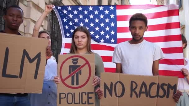 Νέοι μαθητές με διαφορετικά χρώματα του δέρματος διαμαρτύρονται κατά του ρατσισμού και της βίας στο πλαίσιο της σημαίας των ΗΠΑ. Νεαρά αγόρια και κορίτσια κρατούν πλακάτ - χωρίς ρατσισμό, BLM, ελεύθερη ζώνη της αστυνομίας — Αρχείο Βίντεο