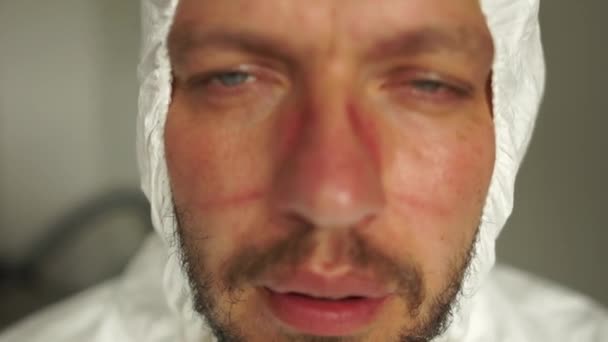 Moe dokter, een jongeman met sporen van een masker op zijn gezicht, rustend, diep ademend. Hard werk van artsen tijdens de pandemie van coronavirus covid-19 — Stockvideo
