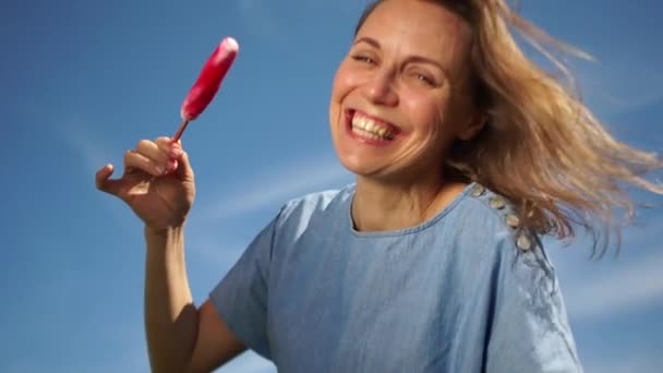 Primer plano de una mujer guapa lamiendo un helado sobre el fondo del cielo azul. La chica en sentimientos alegres. Aire libre, estilo de vida — Vídeos de Stock