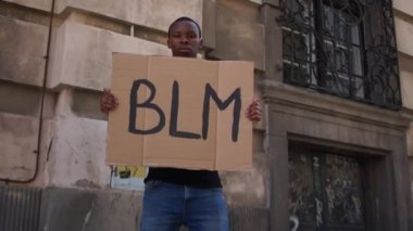 Siyahların hayatı önemlidir. Genç Afro-Amerikan bir adam elinde BLM yazılı bir poster tutuyor. Şiddet ve polis şiddetine karşı protestolar
