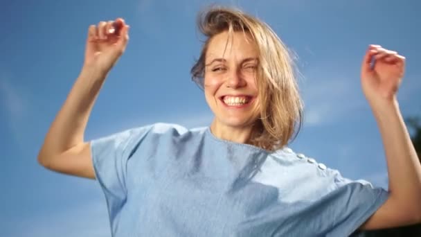 Ritratto soleggiato di una giovane donna con un sorriso dai denti bianchi contro il cielo. Bella ragazza felice in un vestito di denim — Video Stock