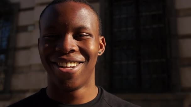 Uomo nero sorridente mentre guarda la macchina fotografica. Ritratto di un giovane afroamericano in t-shirt bianca su city street. Concetto di persone felici, stop rasicm — Video Stock