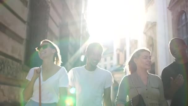 Grupo interracial de estudiantes caminando por la ciudad. Soleado retrato de cuatro jóvenes caminando por la calle. Dos hombres negros y dos mujeres blancas — Vídeos de Stock