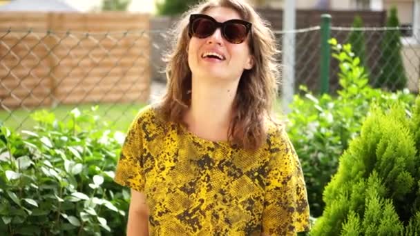 Close portrait of a lovely young woman in sunglasses in her garden. The girl holds clippers in her hands and laughs. Garden work, cutting bushes — Stock Video