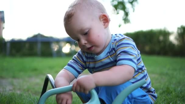 Chiudere upadorable bambino ragazzo versa acqua in un annaffiatoio con un tubo flessibile. Lavoro in giardino, assistente di villaggio, vacanze estive, bambino felice — Video Stock