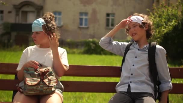 Schulkinder sitzen mit Masken auf dem Kopf auf einer Bank. Video von Fanny nach der Quarantäne. Neue Normalität, Kinder nach Quarantäne-Coronavirus covid-19 — Stockvideo