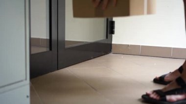 Tanınmayan bir kadın ön kapıyı açar ve kutuyu alır. Kapılara mal teslimatı, kurye servisi. Temassız teslimat, online alışveriş. Coronavirus covid-19 sırasındaki sosyal mesafeler