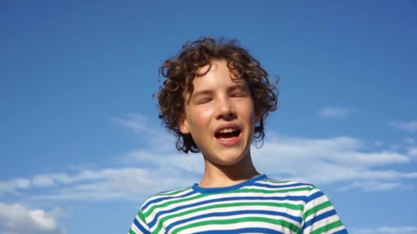 Curly lindo colegial en una camiseta a rayas bosteza una boca abierta con su mano, el niño está aburrido, vacaciones de verano — Vídeos de Stock