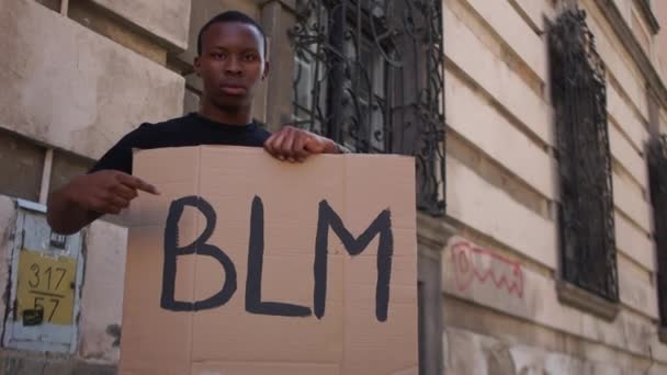 Hombre afroamericano sosteniendo un póster improvisado con la inscripción BLM. Las vidas negras importan, retrato al aire libre. Protestas en Estados Unidos — Vídeo de stock