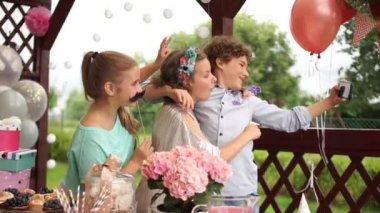 Mutlu çocuklar akıllı telefonu kullanarak selfie çekiyorlar. Doğumgünü partisi açık havada renkli pasta, çikolata ve toplarla