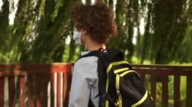 Okulu bitirdikten sonra, okul çocuğu gölün kıyısındaki parka geldi ve maskesini çıkardı. Karantinadan sonra okula dönüyorum. Maskeli çocuk