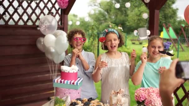 Boldog gyerekek pózolnak a szülőknek fotós kellékekkel egy gyerekünnepen. Boldog születésnapot, gyermek partik szervezése, vendéglátás koncepció — Stock videók