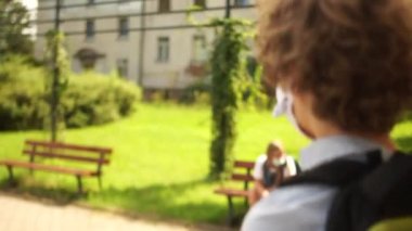 Karantinadan sonra okula, sosyal mesafeye. Maskeli çocuk okuldan çıkıyor ve okul bahçesindeki bir bankta oturuyor. Maskeyi ve tabakları özgürce çıkartıyor. COVID-19 koronavirüs salgını sırasında karantina