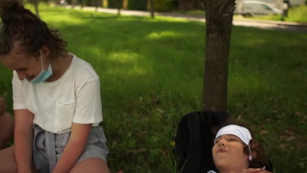 Des adolescents masqués s'assoient sur l'herbe, parlant et riant. Distance sociale, vie post-quarantaine — Video