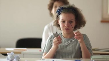 Şirin kıvırcık saçlı bir kız ders sırasında masada otururken gözlük takıyor. Okula geri dön.