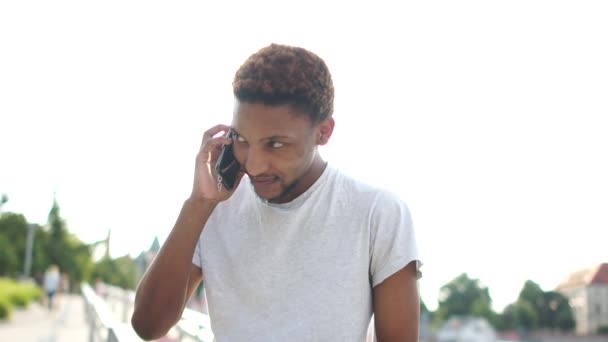 Zwarte student leest berichten op zijn telefoon en lacht. Outdoor portret van een Afro-Amerikaanse man met een smartphone in zijn handen — Stockvideo