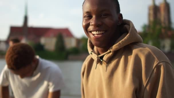 Близкий портрет молодого чернокожего человека. Афроамериканский студент смеется. Близкий портрет на городской улице — стоковое видео
