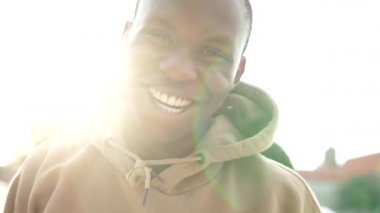 Gülümseyen siyah bir öğrencinin portresi. Adam bej bir kapüşonlu giyiyor. Şehir caddesinde açık hava portresini kapat