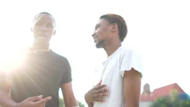 Retrato al aire libre de dos estudiantes negros. Concepto de igualdad y hermandad. Encuentro de dos amigos afroamericanos. Saludo apretón de manos y abrazo — Vídeos de Stock