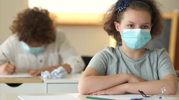 Torna a scuola vigliacco. I bambini in maschere mediche protettive siedono alle loro scrivanie a scuola. Studentessa riccia. Maschera per bambini — Video Stock