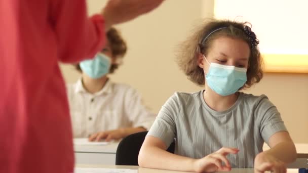 De volta à escola. O professor, de pé na frente da turma, explica um novo tópico. As crianças mascaradas escutam atentamente. Nova normalidade, reabrir escolas — Vídeo de Stock