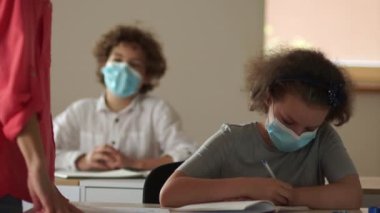 Sınıfın önünde duran öğretmen yeni bir konuyu açıklıyor. Maskeli çocuklar dikkatle dinliyorlar ve yazıyorlar. Yeni normallik, okulları yeniden açmak. Okula dönelim. Çocuklar maske takıyor