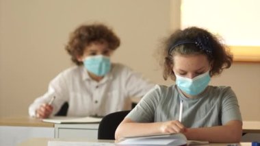 Koruyucu tıp maskeli sınıf arkadaşları, bir oğlan ve bir kız okuldaki masalarında oturuyorlar. Oğlan kızdan bir gazete ister. Okula dön.
