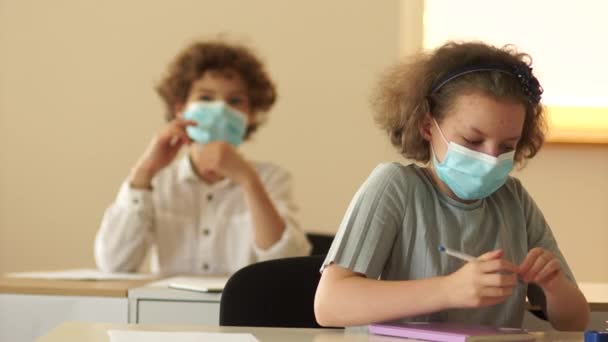 Schulkinder in Masken stehen vom Schreibtisch auf. Ende der Lektion. Neue Normalität, Rückkehr in die Schule nach Quarantäne-Coronavirus covid-19. Wiedereröffnung der Schulen — Stockvideo