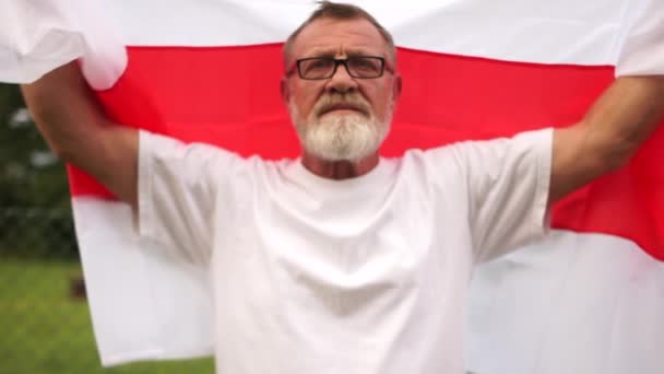 男はベラルーシの旗を保持し、空と太陽の背景に対して長さに彼の腕でそれを伸ばします。ベラルーシでの抗議 — ストック動画