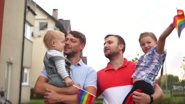 Eşcinsel çift. Çocuklu iki adam öpüşüyor. Evin ve gökyüzünün arka planında LGBT bayrakları tutan iki çocuklu aynı cinsiyetten aile. Evlatlık çocuklar — Stok video