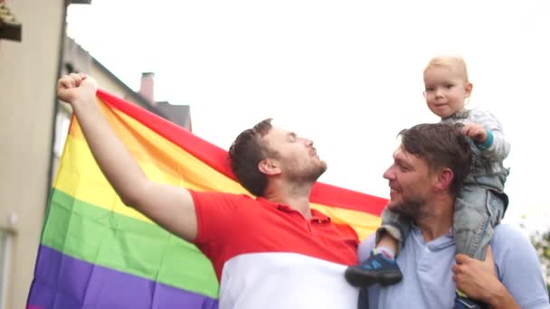 Küçük bir çocuğa sarılan ve LGBT bayrağı taşıyan eşcinsel bir aile. Eşcinsel hakları, homoseksüel evlilik, çocuk evlat edinme. Aynı cinsiyetten çocuklar. — Stok video