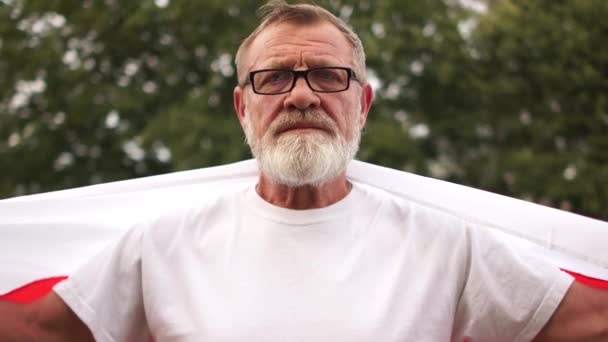 Збільшений портрет сірого пенсіонера з окулярами і бородою з червоним і білим прапором Білорусі. Протест у Білорусі, кольорова революція — стокове відео