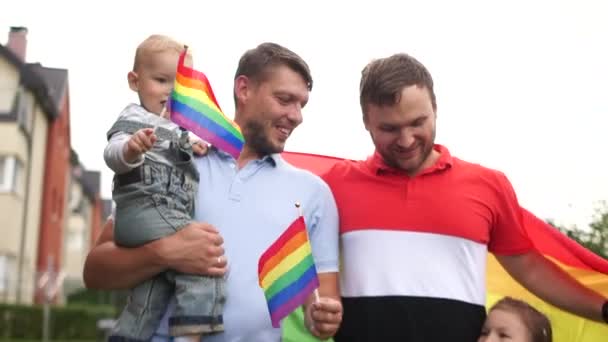 Sebuah keluarga dengan dua ayah. Dua anak, seorang anak laki-laki dan seorang gadis dalam keluarga homoseksual. Potret dekat, anak-anak memegang bendera LGBT. Hari ayah, adopsi anak — Stok Video