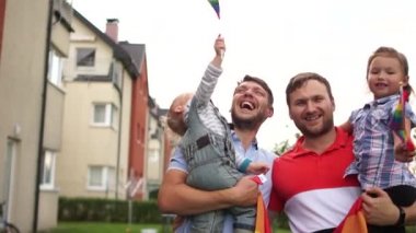 Hoş homoseksüel çift, iki evlatlık çocuklu iki eşcinsel adam. Birbirlerine sarılıp gülüyorlar. Elinde gökkuşağı bayrakları, lgbt topluluğu