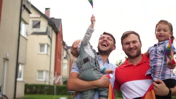 Pasangan homoseksual yang indah, dua pria gay dengan dua anak angkat. Mereka saling memeluk dan tertawa. Memegang bendera pelangi, komunitas lgbt — Stok Video