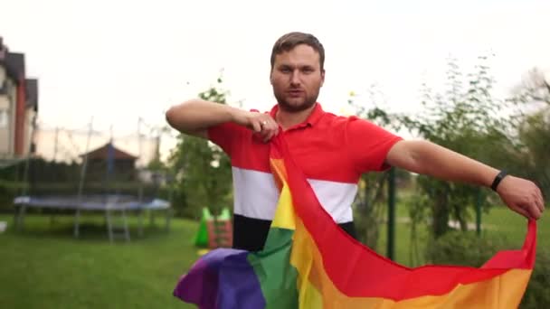 Joven feliz hombre gay tiene ventilador al aire libre y bailando con una gran bandera de arco iris. Comunidad LGBT, desfile gay, derechos gay y tolerancia en la sociedad — Vídeos de Stock