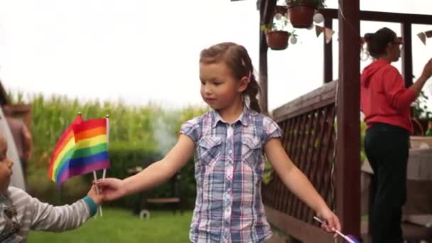 LGBT社区，收养儿童，宽容。孩子们，男孩和女孩，在院子里玩彩虹LGBT旗 — 图库视频影像