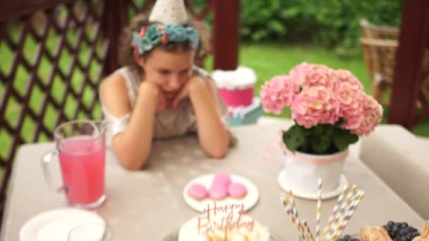 Een verdrietig eenzaam verjaardagsmeisje zit alleen aan een tafel met snoep. Het schoolmeisje liet haar hoofd zakken en is verdrietig dat er niemand naar het verjaardagsfeest kwam. — Stockvideo