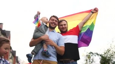 İki çocuklu genç bir homoseksüel aile. Açık havada iki adam, bir çocuk ve bir kız ellerinde LGBT bayrakları tutuyorlar.