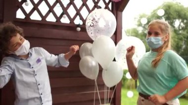 İki genç, bir doğum günü partisinde balonların önünde maske takarak dans ediyor. Sosyal uzaklık, covid-19 koronavirüs salgını sırasında alınan önlemler