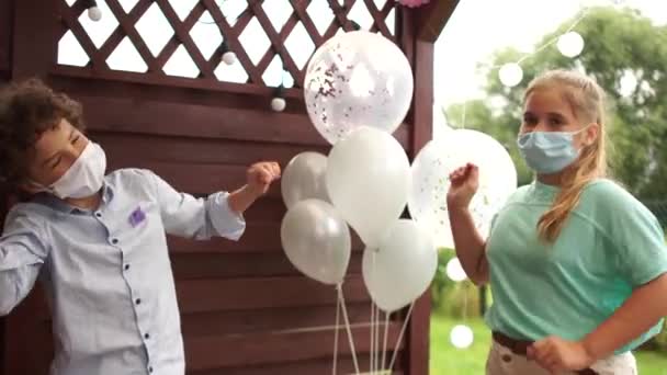 Deux adolescents dansent masqués lors d'une fête d'anniversaire sur fond de ballons. Distance sociale, précautions pendant la pandémie de coronavirus covid-19 — Video