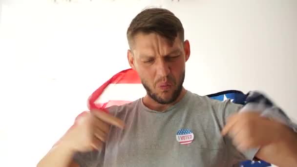 Egy hazafias férfi Voit-táblával a mellkasán áll zászlóval a vállán, mosolyog, és gratulál a választási győzelemhez. Szavazás 2020 Amerikai Egyesült Államok Elnöki — Stock videók