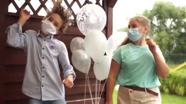 Дитяча вечірка під час пандемії коронавірусу. Двоє підлітків танцюють в масках на день народження на тлі повітряних куль. Соціальне дистанціювання — стокове відео