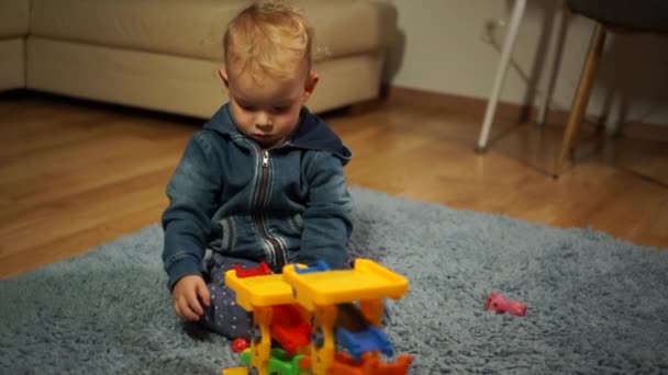 Niño jugando con bloques de construcción en casa o jardín de infantes. Niño feliz es apasionado de jugar con juguete de plástico mientras está sentado en la alfombra — Vídeo de stock